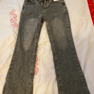 Grå bootcut jeans med hög midja - Snygga grå jeans med bootcut-modell och hög midja. Jeansen har klassisk femficksdesign och är tillverkade i ett mjukt denimtyg. Perfekta för dig som gillar en retrovibe och vill ha ett par jeans som sticker ut lite extra. 