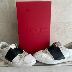 Valentino Garavani vita sneakers - Snygga vita sneakers från Valentino Garavani med bred svart detalj över sidan. Skorna har rund tå, snörning och är tillverkade i skinn. Klassisk och stilren design som passar till det mesta. Kommer med originalröd box.6/10 skick hör av vid frågor 