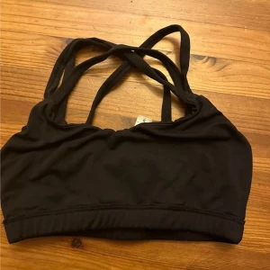 Svart linnetopp från Gina Tricot - Svart linnetopp från Gina Tricot med smala axelband som korsas i ryggen. Toppen är ärmlös och har en tight passform med elastisk nederkant. Perfekt för träning eller som ett basplagg. Tillverkad i mjukt och stretchigt syntetmaterial.