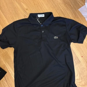 Svart Lacoste piké  - Helt ny. Stolen L passar även M