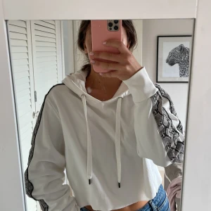 Vit hoodie från Replay - Säljer en vit  hoodie från Replay med coola ormmönstrade detaljer längs ärmarna. Tröjan har huva med snörning och svart Replay-tryck på ryggen. Perfekt för dig som gillar streetstyle och vill sticka ut lite extra.