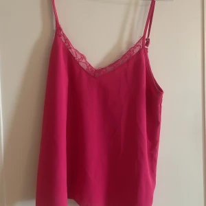 Rosa linnetopp med spetsdetalj - Säljer en snygg rosa linnetopp med tunna axelband och v-ringning dekorerad med spets. Toppen har en lös passform och är tillverkad i ett mjukt, lätt material som känns skönt mot huden.