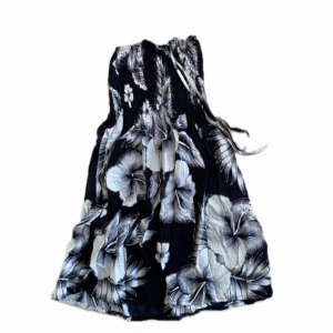Tropisk klänning - En svart och vit blommig klänning med snörning runt nacken jag köpte i Grekland för ett par år sedan. Passar nog en 10-12 åring. Bra kvalitet och i fint skick⭐️⭐️⭐️ Vet inte om något märke då det inte finns någon lapp.