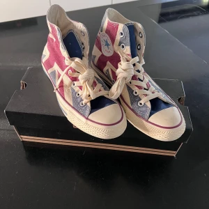 Converse All Star Union Jack High Tops - Snygga Converse All Star high tops med Union Jack-mönster i rött, blått och beige. Klassisk rund tå, vita snören och platt sula. De är helt oanvända.