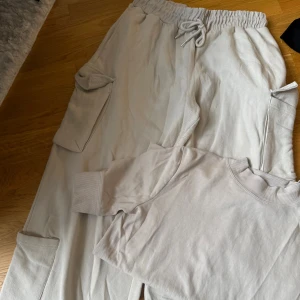 Beige cargopants och t-shirt från Zara - Snygga beige cargopants och t-shirt från Zara med elastisk midja och dragsko. Byxorna har stora fickor på sidorna och är gjorda i mjuk bomullsmix som känns riktigt skön mot huden. Perfekta för en avslappnad och trendig look. 350kr för hela settet 