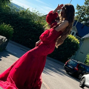 Röd långklänning med spets och puffärm - Säljer en fantastisk röd långklänning med figurnära passform och utsvängd nederdel. Klänningen har vackra spetsdetaljer, blommönster och puffiga långa ärmar som ger en lyxig känsla. Perfekt för bal eller fest, med offshoulder-skärning och romantisk look.