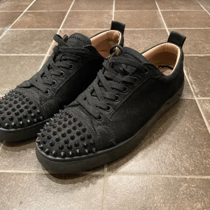 Svarta Louboutin sneakers  - Svarta sneakers från Christian Louboutin i mocka med svarta nitar på tån och klassisk röd sula. De tvättas självklart innan jag skickar. De finns vissa skador på insidan av skorna men det är inget man ser, det finns också en liten fläck på utsidan vilket det finns bild på dock syns den inte så mycket. Priset kan diskuteras vid snabb affär och tveka inte på att höra av dig