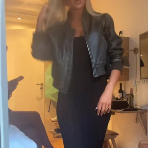 Svart bomberjacka i skinnlook - Säljer en svart bomberjacka med skinnlook och ribbade muddar. Jackan är croppad och har dragkedja framtill. Den har en klassisk bomberform med lite loose passning och långärmade ärmar. Perfekt för dig som vill ha en cool och tidlös jacka. Så populär och slutsåld, finns inte att köpa längre.