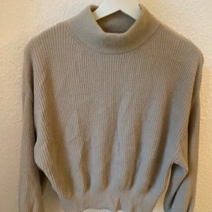 Beige stickad polotröja Pull&Bear - Beige stickad polotröja från Pull&Bear med ribbad struktur och hög hals. Tröjan har lång ärm och en lite loose passform, perfekt för lager på lager. Enkel och stilren design som funkar till många olika looks. Kan passa även storlek S. Lite nopprig.