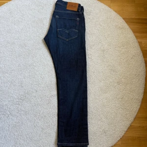 Mörkblå Replay Rocco jeans comfort fit - Snygga mörkblå jeans från Replay, modell Rocco med comfort fit. Klassisk femficksdesign, kontrastsömmar och diskret Replay-logga på fickan. Jeansen har rak passform och är tillverkade i slitstarkt denimtyg. Perfekta för en avslappnad och stilren look. Använt de 2 gånger, storlek 31/30