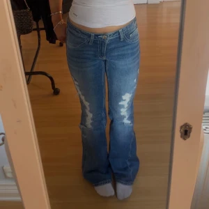 Blå bootcut jeans från Gina Tricot - Snygga blå bootcut jeans från Gina Tricot med slitna detaljer framtill. Klassiska jeans med medel midja och coola sömmar på bakfickorna. Jeansen är i denim och har en knappstängning framtill. Använda en gång, ingen fläckar eller hål (förutom där de ska vara hål) 