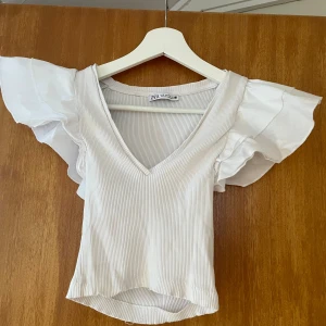 Vit topp - Supersöt vit ribbad topp från Zara med djup v-ringning och stora volangärmar.