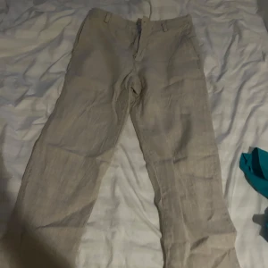 Beiga linnebyxor med rak passform - Snygga beiga linnebyxor med klassisk rak passform och hällor för bälte. Byxorna har diskreta sidfickor och stängs med dragkedja och knapp. Perfekta för en chill och stilren look under varmare dagar.