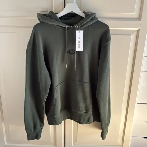 Mörkgrön hoodie från Han Kjøbenhavn - Snygg mörkgrön hoodie från Han Kjøbenhavn med broderad logga på bröstet. Tröjan har huva med snörning, stor magficka och ribbade muddar vid ärmslut och nederkant. Storlek M. Helt ny och etiketten sitter kvar i plagget. Nypris 1500 DK, motsvarar ca 2200kr.