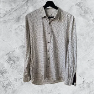 Rutig skjorta från Barbour slim fit - Säljer en snygg rutig skjorta från Barbour i slim fit-modell. Skjortan är vit med tunna rutor i lila och blått, har långa ärmar och klassisk krage. Perfekt för dig som gillar stilrena och tidlösa plagg. Knappar framtill och mjukt bomullsmaterial.