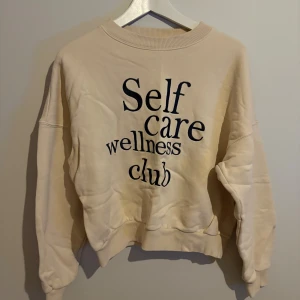 Beige sweatshirt från H&M med tryck - Beige sweatshirt från H&M med svart text 'Self care wellness club' på framsidan. Tröjan har rund hals, ribbade muddar och är långärmad. Tillverkad i mjuk bomullsmix som är perfekt för chill dagar.