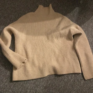 Beige ribbad polotröja - Snygg beige ribbad polotröja med hög hals och lång ärm. Tröjan är använd enstaka gånger och är i storlek S