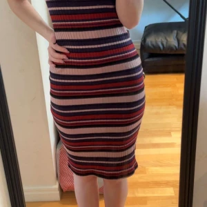 Randig ribbad klänning från NA-KD - Säljer en tight, ribbad klänning från NA-KD i storlek XS. Klänningen är knälång och har horisontella ränder i lila, rött, rosa och mörkblått. Den är ärmlös och har en figurnära passform som framhäver siluetten. Perfekt för dig som gillar färg och mönster!