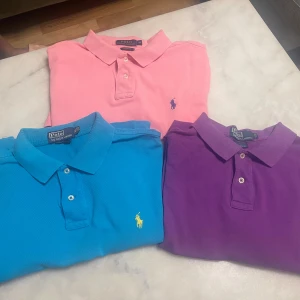 3 färgglada pikétröjor från Ralph Lauren - Tre klassiska pikétröjor från Ralph Lauren i färgerna rosa, blå och lila. Alla har broderad logga på bröstet, krage och knäppning framtill. Perfekta för dig som vill sticka ut med färg och stil. Materialet är mjuk bomull som andas. Tröjornas modell är från många år tillbaka. Säljer individuellt också för 200kr styck och alla 3 för 500. Vid frågor ställ gärna!!
