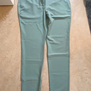 Mintgröna chinos från Tendency, M - Snygga mintgröna chinos från Tendency i storlek M. Byxorna har raka ben, klassiska fickor fram och bak, bälteshällor och stängs med dragkedja och knapp. Perfekta för dig som gillar stilrena och fräscha färger.