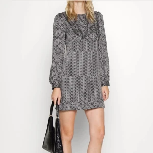 Svartvit mönstrad kortklänning - Snygg svartvit kortklänning med lång ärm och grafiskt rutigt mönster. Klänningen har rund halsringning och en rak passform som ger en stilren look. Perfekt för dig som gillar en enkel men trendig stil.