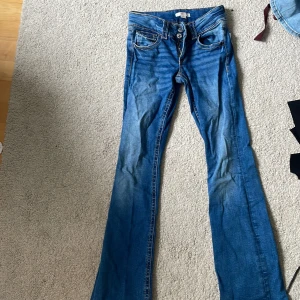 Blå bootcut jeans med slitningar - Snygga blå jeans med bootcut-modell och klassiska fickor både fram och bak. Jeansen har en lätt tvättad look med markerade sömmar. 