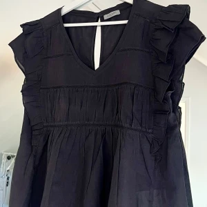 Blus från Hunkydory - Supersöt mörkgrå  blus från Hunkydory med v-ringning, volangdetaljer längs axlarna och ärmlös design. Är aldrig använd. Storlek M.