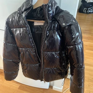 Svart glansig pufferjacka från Nelly - Säljer en svart glansig pufferjacka från Nelly i storlek XS. 