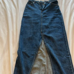 Lång jeanskjol med slits - Snygg lång jeanskjol i klassisk blå denim med hög midja, framfickor och bakfickor. Kjolen har en markerad slits framtill som ger en cool vibe. Perfekt att styla med sneakers eller boots för en trendig look. Från monki. Skriv gärna för frågor eller bara intresserad❤️