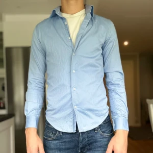 Ljusblå skjorta från Dressmann - Säljer en stilren ljusblå skjorta från Dressmann i slim fit-modell. Skjortan har klassisk krage, långa ärmar och knäppning framtill. Perfekt för dig som gillar en enkel och fräsch look. Storleken är XS men är stor i storleken! Sitter som s-m,han på bilden är 180 bara att skriva till mig om ni har några funderingar!