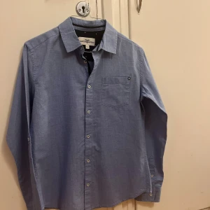 Blå skjorta från Hampton Republic - Snygg blå skjorta från Hampton Republic. Storlek 164/kids. Använd fåtal gånger, mycket bra skick. Snygga knappdetaljer på ärmarna