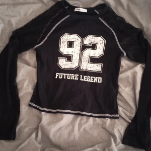 Svart meshtröja Future Legend 92 - Svart långärmad meshtröja från Funky Buddha med tryck '92 Future Legend' framtill. Tröjan har tight passform, kontrastsömmar och är tillverkad i syntetmaterial. Ärmarna är helt i mesh vilket ger en liten fin, häftig detalj🩷 Den är i storlek L men jag skulle säga att den är som en S tröja från Gina ungefär✌️
