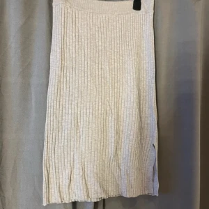 Beige ribbad kjol från Gina Tricot - Superfin beige ribbad kjol från Gina Tricot med slits på sidan. Kjolen är stickad och har en mjuk, stretchig midja. Perfekt för dig som gillar en enkel men ändå snygg look. Lång modell som passar till många olika stilar.