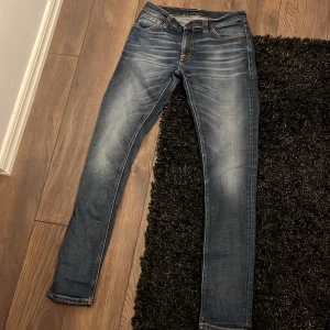 Nudie jeans 28/32 - Snygga blå jeans från Nudie Jeans med klassisk orange söm och vågig brodyr på bakfickorna. Modellen är skinny fit med låg till normal midja och tillverkad i mjukt denimtyg. Perfekta för dig som gillar en smal siluett och coola detaljer. Pris inte huggit i sten