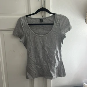 Grå ribbad topp från SHEIN - En enkel och stilren grå ribbad topp från SHEIN i storlek XS. Toppen har rund halsringning och korta ärmar, perfekt att matcha med jeans eller kjol. Materialet är mjukt och stretchigt för en bekväm passform.