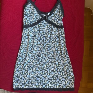 Blommig kortklänning från H&M Divided - Supersöt kortklänning från H&M Divided med blått och vitt blommönster på svart botten. Klänningen har spetsdetaljer vid bysten och tunna axelband. Perfekt för en somrig look med en feminin touch.