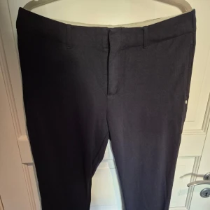 Byxor Scotch & Soda L - Stilrena svarta kostymbyxor från Scotch & Soda i storlek L. Byxorna har raka ben, bälteshällor och diskreta bakfickor. Materialet är mjukt och stretchigt för extra komfort. Perfekta för en clean och dressad look. Är väldigt mörkblåa, nästan svarta. 