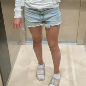 Ljusblå jeansshorts från H&M Divided - Säljer ett par ljusblå jeansshorts från H&M Divided i klassisk femficksmodell. De är högmidjade med råa, fransiga benslut och dragkedja framtill. Perfekta för sommaren och har en loose fit som ger en avslappnad vibe.