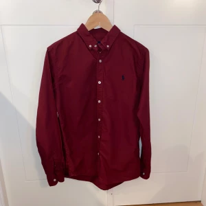 Vinröd skjorta från Ralph Lauren - Snygg vinröd skjorta från Ralph Lauren med den klassiska Ralph lauren märket på bröstet.  Storlek M