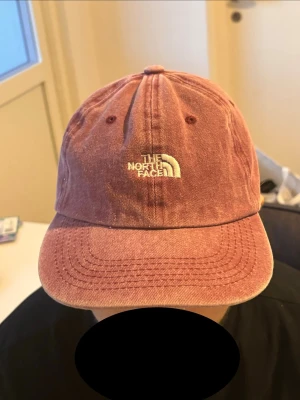  The North Face keps  - Säljer en vinröd keps från The North Face med böjd skärm och broderad vit logga framtill. Kepsen har justerbart spänne bak.