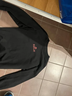 Svart sweatshirt från Replay - Svart sweatshirt från Replay med röd logotyp och ett litet emblem på bröstet. Tröjan har rund halsringning och långa ärmar med ribbade muddar. Enkel och stilren design som passar till det mesta.