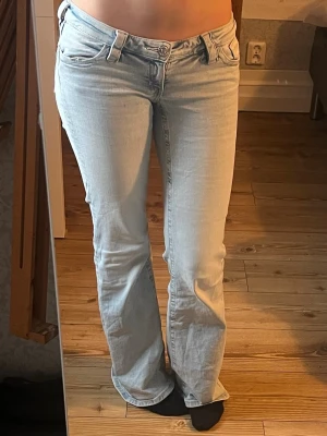 Ljusblå bootcut jeans - Säljer ett par ljusblå bootcut jeans med klassisk femficksdesign och låg midja. Jeansen har en snygg tvätt och raka ben som går ut lite nedtill. Perfekta för dig som gillar en avslappnad men ändå trendig look. Srl m i gina 14+ men små i storleken passar om du är 38 eller 36