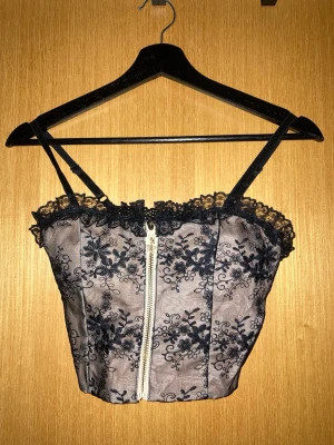 topp med lace och blommor - sjukt söt topp med svart lace och blommor och hudfärgat tyg under. har en guldig dragkedja med en stjärna fram. dragkedjan går inte att dra ner hela vägen, men det spelar ingen roll för att få på sig den. väldigt stretchigt see-through material bak. 