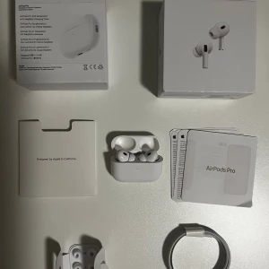 Apple AirPods Pro 2 trådlösa hörlurar - Säljer ett par vita Apple AirPods Pro 2 med laddningsetui och originalförpackning. Hörlurarna har in-ear design, brusreducering och levereras med laddkabel och manualer. Perfekta för musik, samtal och träning tack vare den smidiga och stilrena designen.