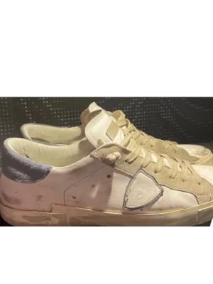 Vita sneakers från Philippe Model - Snygga vita sneakers från Philippe Model med beige mockadetaljer och ljusblå häl. Skorna har snörning, rund tå och platt sula. Perfekta för en avslappnad och trendig stil.