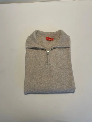Beige stickad halvzip från Ryvyls - Beige stickad tröja från Ryvyls med halv dragkedja och hög krage. Tröjan har lång ärm och ribbade muddar vid ärmslut och nederkant. Perfekt för lager på lager och enkel att matcha med olika stilar.