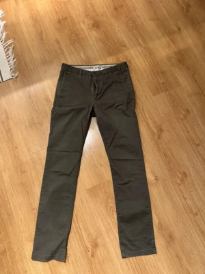 Olivgröna chinos från acne - Snygga olivgröna chinos från Acne i rak modell. Byxorna är tillverkade i bomull med lite elastan för extra komfort. Perfekta för en clean och stilren look. Klassisk design med fickor fram och bak.