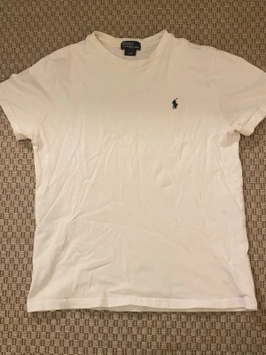Vit t-shirt från Polo Ralph Lauren - Klassisk vit t-shirt från Polo Ralph Lauren med broderad marinblå logga på bröstet. T-shirten har rund halsringning och korta ärmar. Perfekt basplagg i mjuk bomull som funkar till allt. Storlek 10-12år
