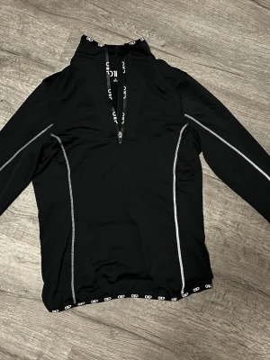 Svart träningströja från OTP - Svart långärmad träningströja från OTP med halv dragkedja fram till. På ryggen finns även en mobil ficka. 