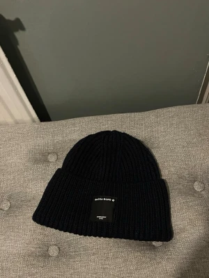 Mörkblå ribbstickad mössa Björn Borg - Mörkblå ribbstickad mössa från Björn Borg med uppvikt kant och en svart etikett framtill. Klassisk modell som passar perfekt till kalla dagar. Tillverkad i mjukt och värmande material.